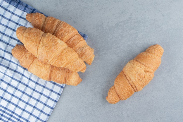 Tres croissants apilados sobre la toalla con un croissant en el fondo de mármol. Foto de alta calidad