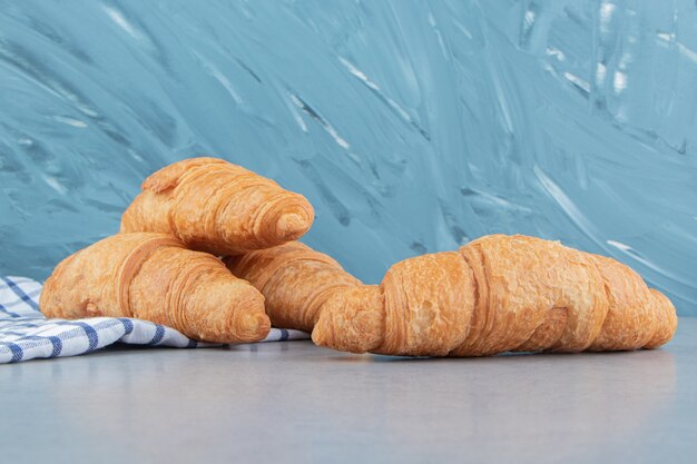 Tres croissants apilados sobre la toalla con un croissant en el fondo de mármol. Foto de alta calidad