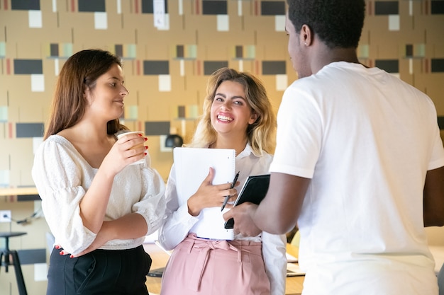 Tres diseñadores alegres de pie juntos y discutiendo el trabajo