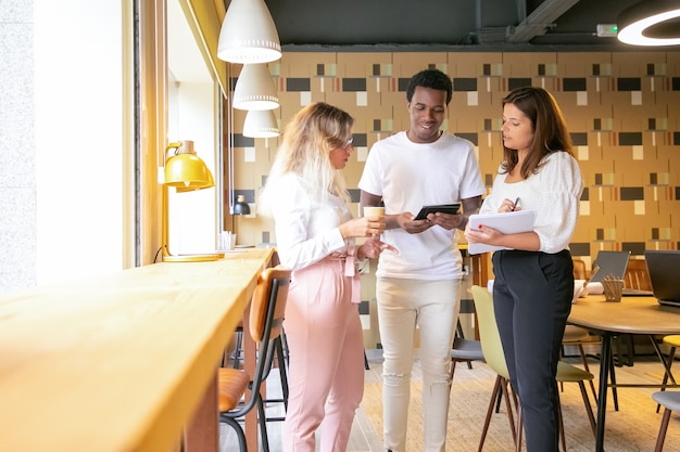 Foto gratuita tres diseñadores de contenido de pie en el interior y discutiendo el diseño