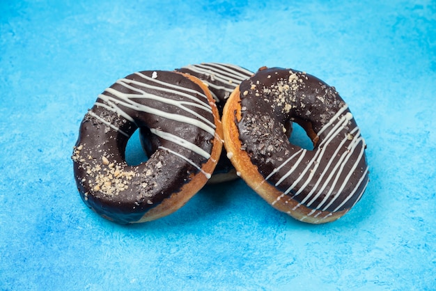 Foto gratuita tres donas de chocolate aisladas sobre superficie azul.