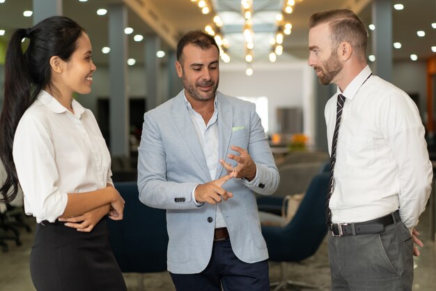 Tres empresarios positivos hablando en el vestíbulo de la oficina