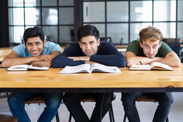 Tres estudiantes de contenido acostado en el escritorio y mirando a la cámara