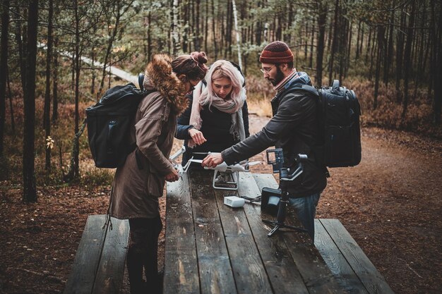 Tres estudiantes están arreglando un dron roto usando una mesa en el parque forestal de otoño.