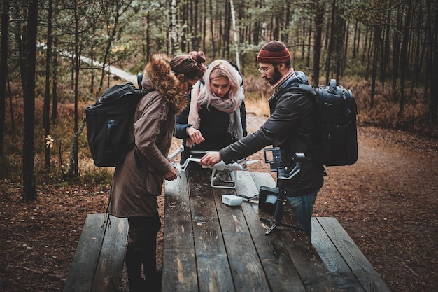 Tres estudiantes están arreglando un dron roto usando una mesa en el parque forestal de otoño.