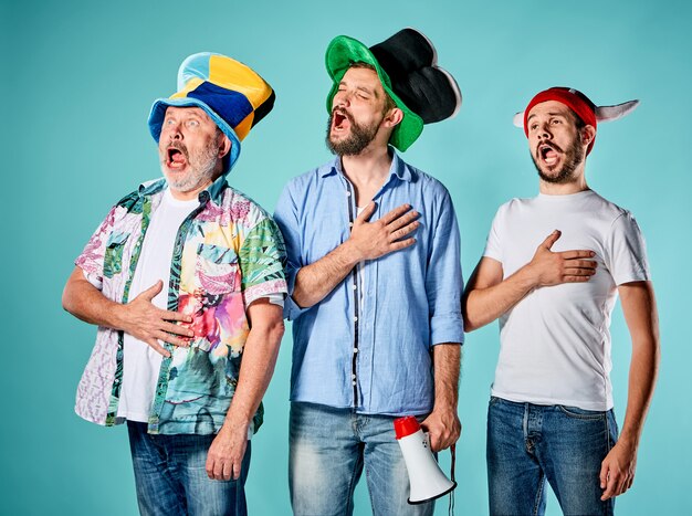 Los tres fanáticos del fútbol cantando el himno nacional sobre azul