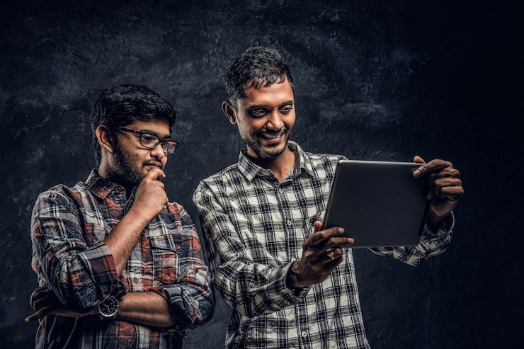 Foto gratuito tres felices amigos indios con ropa informal se paran en un abrazo y se toman selfie en un smartphone. foto de estudio contra una pared oscura