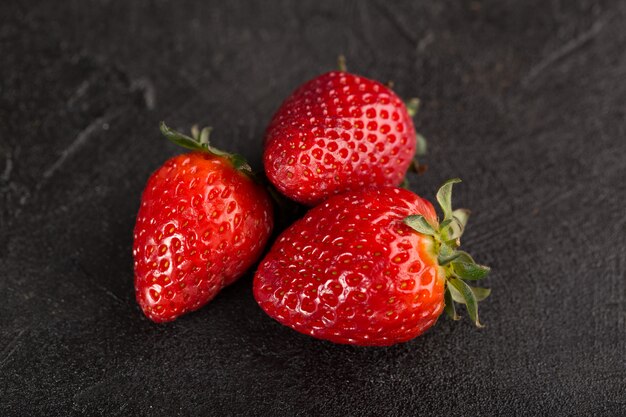 Tres fresas rojas suaves frescas aisladas sobre piso oscuro