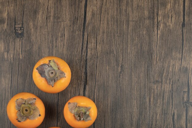 Tres frutos de caqui maduros colocados sobre la superficie de madera