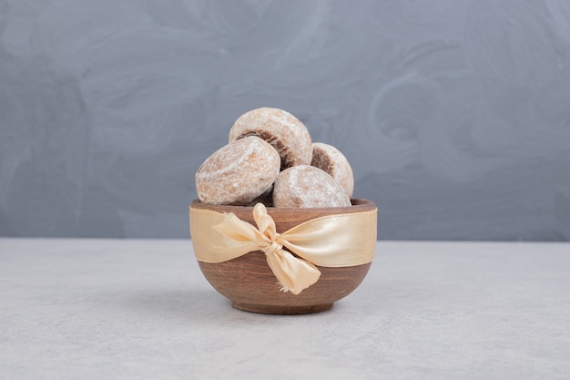 Tres galletas dulces con lazo dorado en tazón de madera