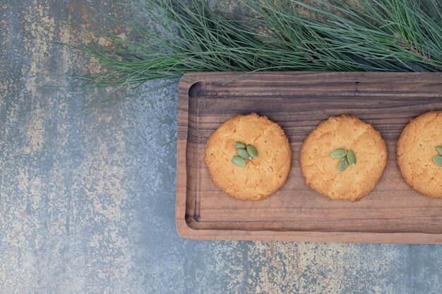 Tres galletas dulces con semillas de calabaza sobre tabla de madera.