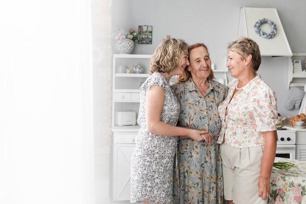 Tres generaciones mujeres juntas y sonrientes en casa.