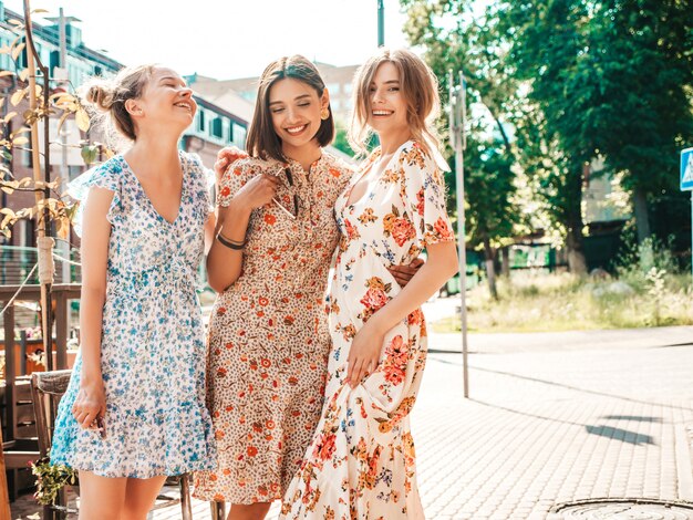 Tres hermosas chicas sonrientes en vestido de verano de moda posando en la calle