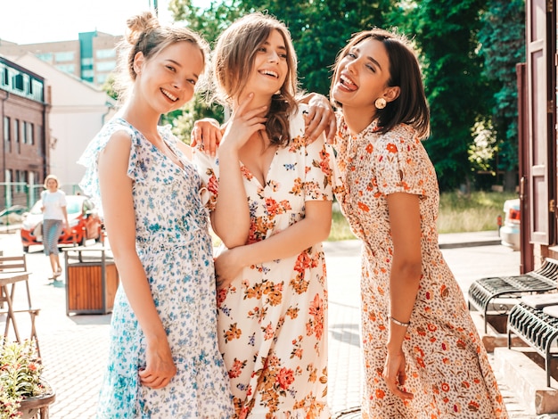 Tres hermosas chicas sonrientes en vestido de verano de moda posando en la calle