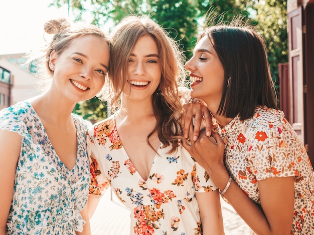 Tres hermosas chicas sonrientes en vestido de verano de moda posando en la calle