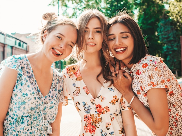 Tres hermosas chicas sonrientes en vestido de verano de moda posando en la calle