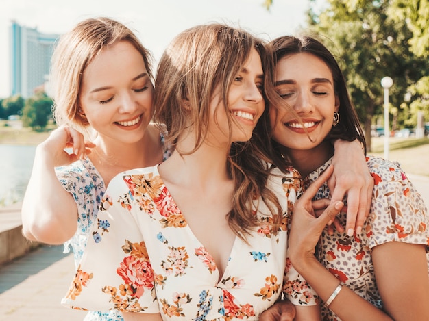 Tres hermosas chicas sonrientes en vestido de verano de moda posando en la calle