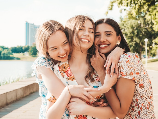 Tres hermosas chicas sonrientes en vestido de verano de moda posando en la calle