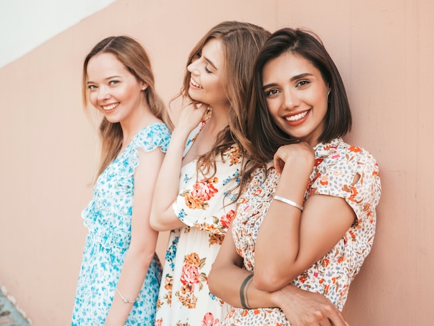 Tres hermosas chicas sonrientes en vestido de verano de moda posando en la calle