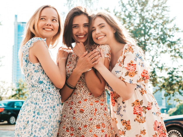 Tres hermosas chicas sonrientes en vestido de verano de moda posando en la calle