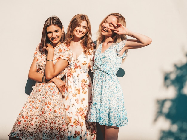 Tres hermosas chicas sonrientes en vestido de verano de moda posando en la calle