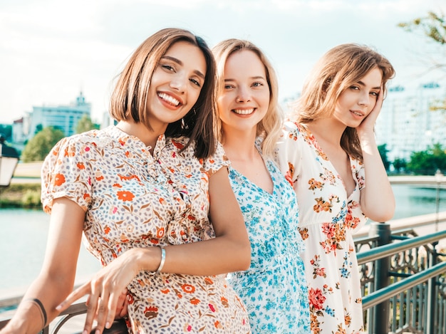 Tres hermosas chicas sonrientes en vestido de verano de moda posando en la calle