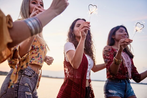 Tres hermosas mujeres divirtiéndose con bengalas en la playa