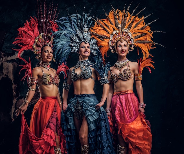 Foto gratuita tres hermosas mujeres jóvenes con trajes tradicionales de carnaval brasileño están posando para el fotógrafo en el estudio.