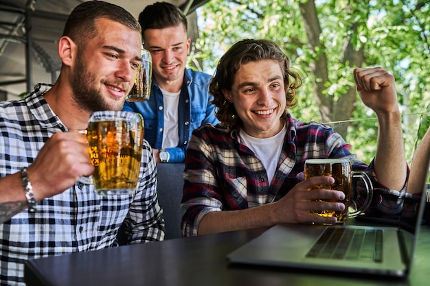Tres hombres guapos viendo fútbol en un pub y bebiendo cerveza.