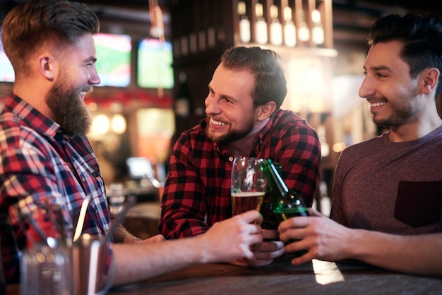 Tres hombres sonrientes bebiendo cerveza en el pub