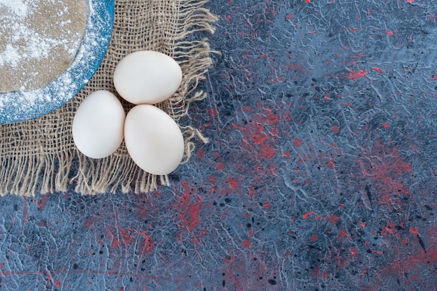 Tres huevos de gallina frescos crudos con masa sobre una tela de saco.