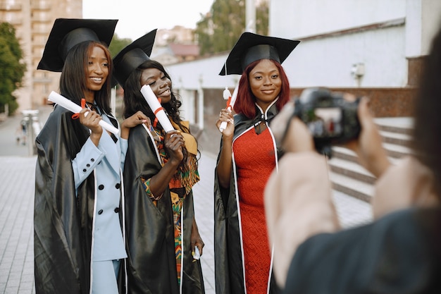 Tres jóvenes estudiantes afroamericanas vestidas con toga negra de graduación. Mujeres posando para una foto