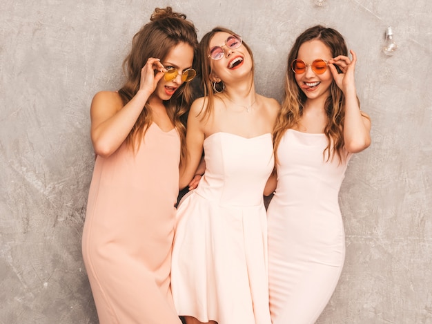 Tres jóvenes hermosas chicas sonrientes en moda rosa claro vestidos de verano. Sexy mujer despreocupada posando. Modelos positivos en gafas de sol redondas divirtiéndose