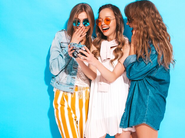 Tres jóvenes hermosas chicas sonrientes en ropa casual de verano de moda y gafas de sol. Sexy mujer despreocupada posando. Tomar fotos en cámara retro