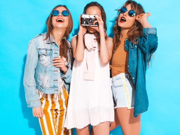 Tres jóvenes hermosas chicas sonrientes en ropa casual de verano de moda y gafas de sol. Sexy mujer despreocupada posando. Tomar fotos en cámara retro