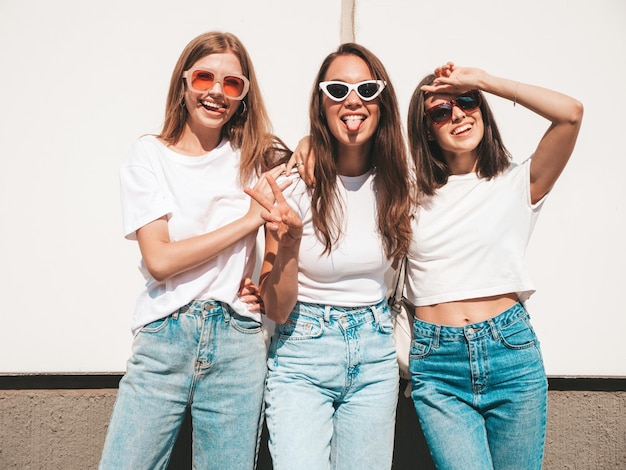 Tres jóvenes hermosas mujeres hipster sonrientes con la misma ropa de verano de moda Mujeres sexys y despreocupadas posando en el fondo de la calle Modelos positivos divirtiéndose con gafas de sol Abrazando Alegre y feliz