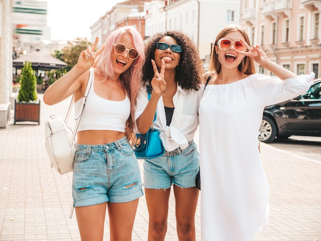 Tres jóvenes hermosas mujeres sonrientes en ropa de verano de moda Mujeres multirraciales despreocupadas sexy posando en el fondo de la calle Modelos positivos divirtiéndose en gafas de sol Alegre y feliz