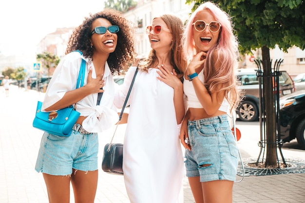 Tres jóvenes hermosas mujeres sonrientes en ropa de verano de moda Mujeres multirraciales despreocupadas sexy posando en el fondo de la calle Modelos positivos divirtiéndose en gafas de sol Alegre y feliz