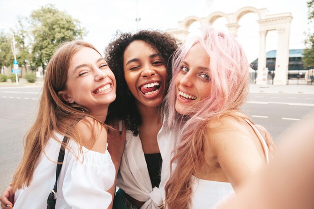 Tres jóvenes hermosas mujeres sonrientes en ropa de verano de moda Mujeres multirraciales despreocupadas sexy posando en el fondo de la calle Modelos positivos divirtiéndose en gafas de sol Alegre y feliz