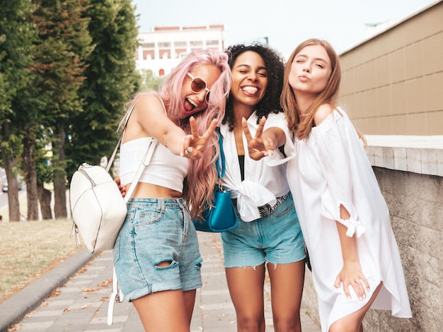 Tres jóvenes hermosas mujeres sonrientes en ropa de verano de moda Mujeres multirraciales despreocupadas sexy posando en el fondo de la calle Modelos positivos divirtiéndose en gafas de sol Alegre y feliz