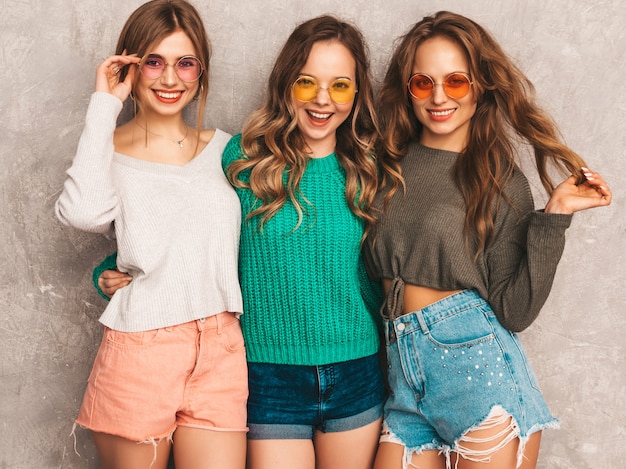 Foto gratuita tres jóvenes hermosas sonrientes hermosas chicas en ropa de moda de verano. sexy mujer despreocupada posando. modelos positivos divirtiéndose en gafas de sol redondas