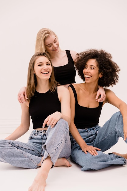 Tres jóvenes mujeres interraciales con ropa informal se ríen pasando tiempo juntas con fondo blanco Estilo de vida étnico diverso