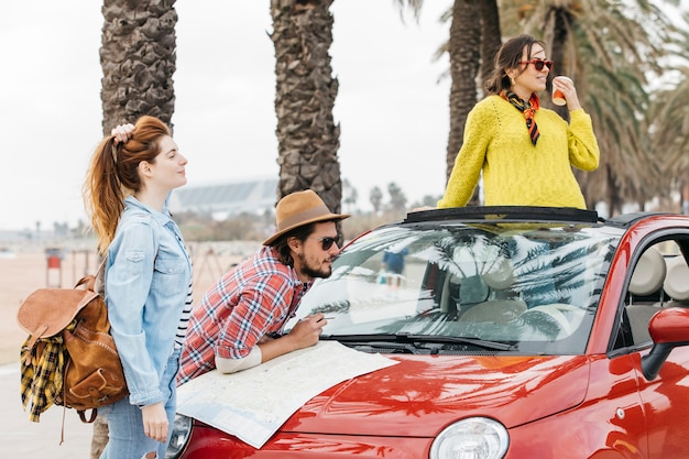 Tres jóvenes de pie cerca de un coche con un mapa de carreteras