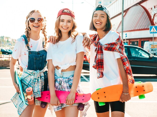 Tres jóvenes sonrientes hermosas chicas con patinetas coloridas centavo.