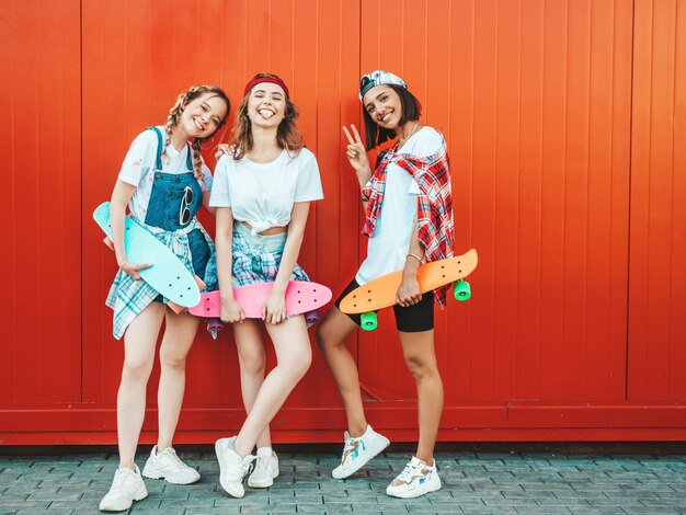 Tres jóvenes sonrientes hermosas chicas con patinetas coloridas centavo.