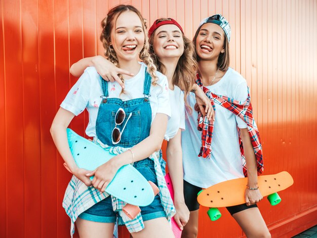 Tres jóvenes sonrientes hermosas chicas con patinetas coloridas centavo.