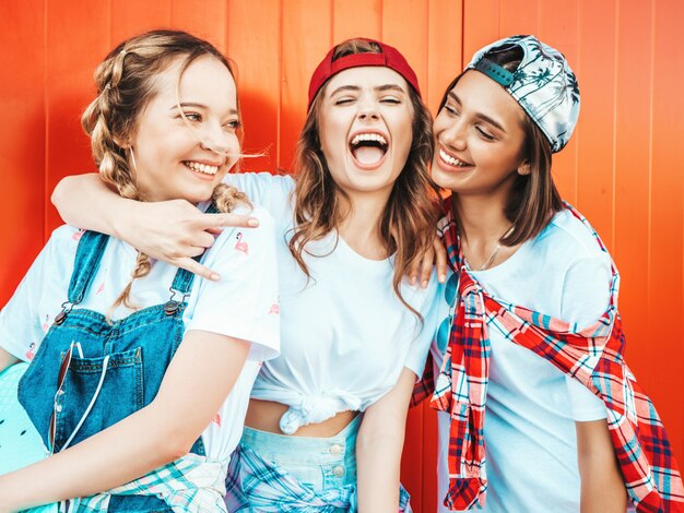 Tres jóvenes sonrientes hermosas chicas con patinetas coloridas centavo.