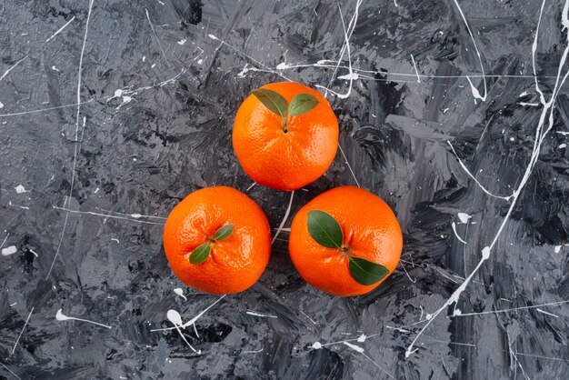 Tres jugosas frutas de mandarina con hojas sobre la superficie de mármol.