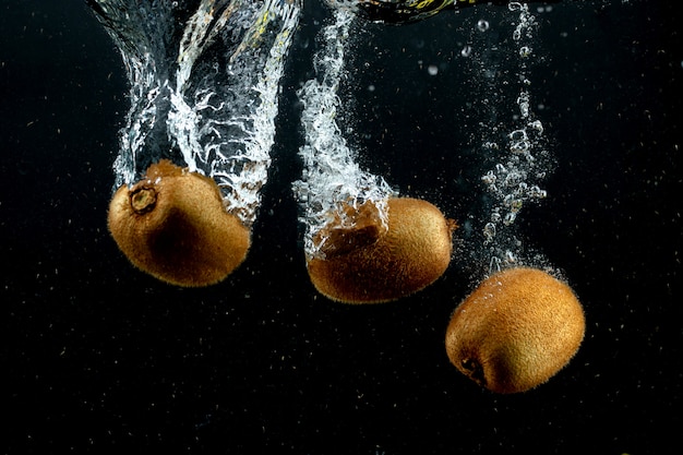 Tres kiwis chapoteando en el agua en fondo negro