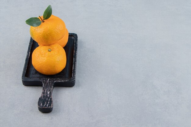 Tres mandarinas frescas sobre tabla de cortar negra